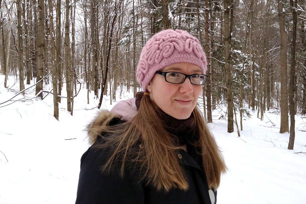 Katherine Guttman in her woods wearing a brainy hat. Happier Place