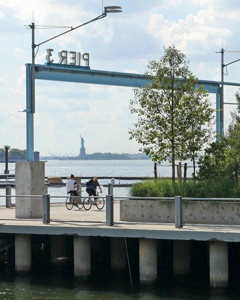 Cyclists on Pier 3 in Brooklyn Bridge Park with Statue of Liberty in the distance.
