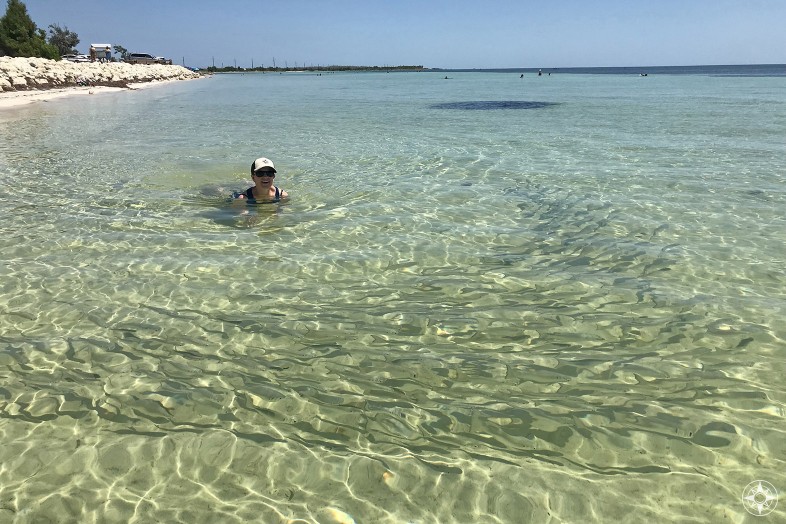 School of fish swimming around woman with Happier Place burlap hat in skinny clear water of Loggerhead Beach on Bahia Honda Key in Florida