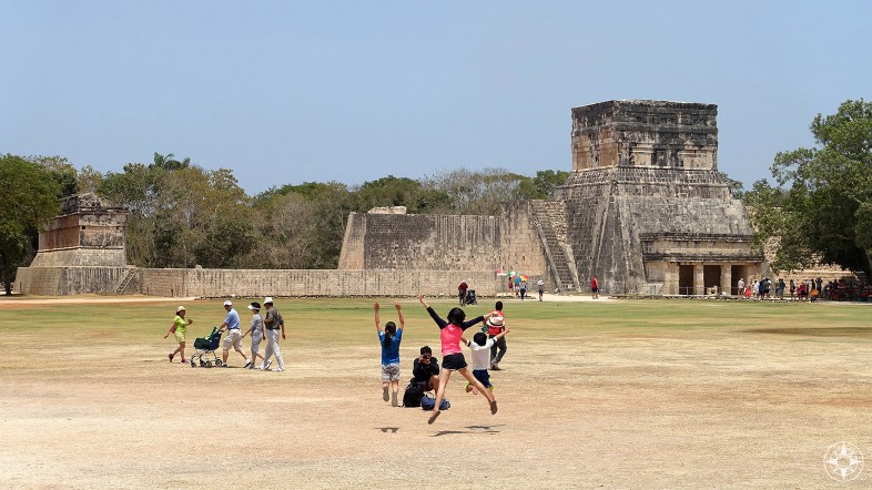 Kids jumping for photographer in front of El Juego de Pelota (Great Ball Court) and Temple of the Jaguars, Chichen Itza, Mexico