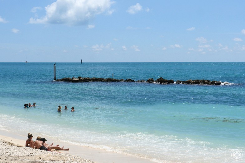 people on the beach and in the blue Key West water, rock wall inviting fish and birds and snorkelers