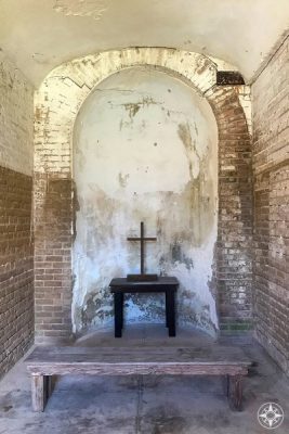 Bench, table and cross in nook inside civil war era Fort Zachary Taylor.