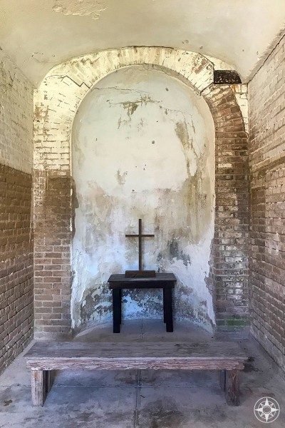 Bench, table and cross in nook inside civil war era Fort Zachary Taylor.