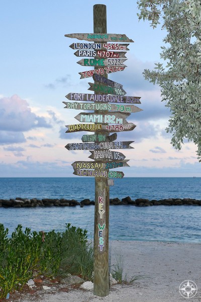 Iconic wooden destinations sign post, Miami, London, New York City, Fort Zachary Taylor Park, Key West, beach, at dusk, Happier Place 