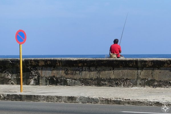 Red and blue traffic sign, man fishing and the sky - Maleón wall, Havana