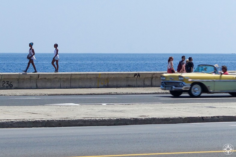 girls walking on seawall, people walking on sidewalk, classic car convertible, blue sea