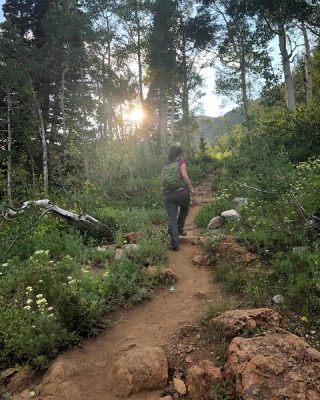 Lost Gorge Mysteries author hiking up a mountain trail above Alta Ski Resort, among trees and wildflowers with her trusted day pack.