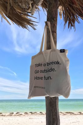 Take a break, go outside, have fun, Happier Place cotton shoulder bag hanging from beach shack, on the beach where Clearwater Beach changes to Caladesi