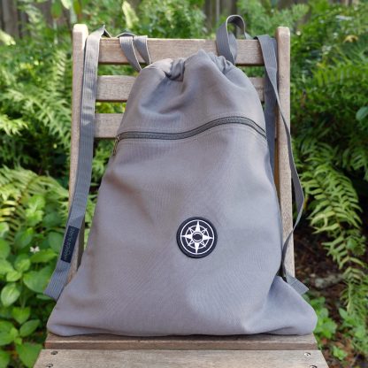Happier Place canvas backpack, cinch bag with shoulder straps, grey, black compass logo patch, shoulder straps